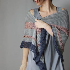May include: A grey and pink striped shawl with a dark blue lace trim. The shawl is draped over the shoulders. The shawl has a knitted design with a lace pattern.