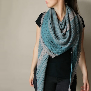 Peut inclure: Un châle tricoté bleu sarcelle et gris avec des motifs de dentelle et de texture complexes. Le châle est drapé sur les épaules, mettant en valeur le design détaillé et le dégradé de couleurs. Les bords ont une bordure festonnée.