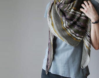 Könnte beinhalten: Ein grauer, olivgrüner und violetter Strickschal mit gelben und weißen Akzenten. Der Schal ist über die Schultern drapiert und zeigt sein kompliziertes Muster und seine Textur. Der Schal hat eine dreieckige Form.