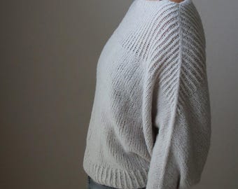 Può includere: Un maglione lavorato a maglia grigio chiaro con scollo a barchetta e maniche lunghe. Le maniche presentano un motivo a coste diagonali e il maglione ha un orlo a coste. Il colore morbido e neutro lo rende un capo versatile.