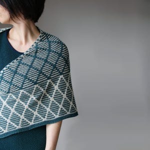 May include: A teal and cream-coloured shawl with a geometric diamond pattern. The shawl is draped over the shoulders, showcasing the intricate knit design. The colour palette is a mix of teal and cream, creating a visually appealing accessory.