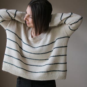 Könnte beinhalten: Cremefarbener Pullover mit horizontalen marineblauen Streifen. Der Pullover hat einen Rundhalsausschnitt und lange Ärmel. Das Strickware ist eine lockere Passform, geeignet für Freizeitkleidung.