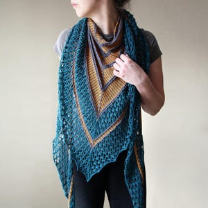 May include: A teal and gold knitted shawl with a geometric design. The shawl features a lacy, openwork pattern along the edges and a chevron pattern in the center. The color scheme includes teal, gold, and gray.