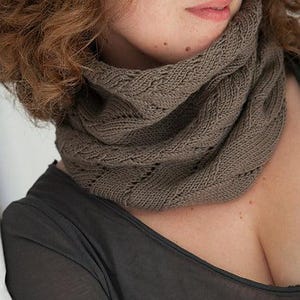 Könnte beinhalten: Ein gestrickter Rundschal in einem neutralen Taupe-Ton. Der Schal ist aus einem weichen, strukturierten Garn mit einem detaillierten Stichmuster gefertigt. Das Design weist eine Rippenstruktur und ein dekoratives Lochmuster auf. Dieses Accessoire ist für kaltes Wetter geeignet.
