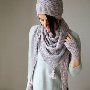 May include: A lilac knitted winter set comprising a hat, scarf, and fingerless gloves. The scarf features tassels. The set is made from a soft, textured yarn, ideal for cold weather. The hat and gloves have a diamond pattern.