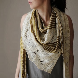 May include: A cream and olive green knitted shawl with a lace edge. The shawl is draped around the shoulders and neck. The shawl has a striped pattern in olive green and cream.