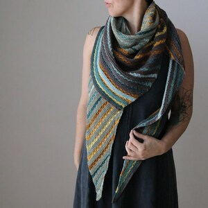 May include: A hand-knitted shawl in shades of teal, brown, and yellow. The triangular shawl features a striped pattern with textured details. The soft, warm accessory is draped over the shoulders.
