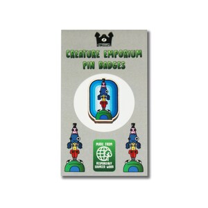 May include: Three wooden pin badges featuring a colorful creature with a blue hat, red shirt, and yellow hair. The badges are made from responsibly sourced wood and are part of the Creature Emporium Pin Badges collection.
