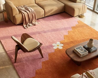 May include: A contemporary living room with a tan sectional sofa, a wooden chair with a cream cushion, and a low wooden coffee table. A colourful rug with a flower design and a geometric pattern in shades of pink and orange adds a vibrant touch to the space.