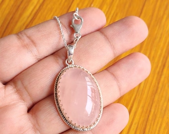 May include: A silver necklace featuring an oval, polished rose quartz pendant. The pink gemstone is set in a decorative silver frame and hangs from a delicate chain. The clasp is visible at the top of the chain.