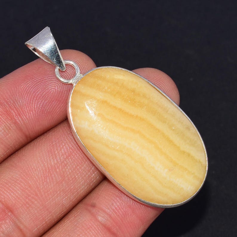 May include: An oval pendant with a silver-coloured metal frame. The pendant has a light yellow stone with a striped pattern. The bail is also silver-coloured. This is likely a piece of jewellery.