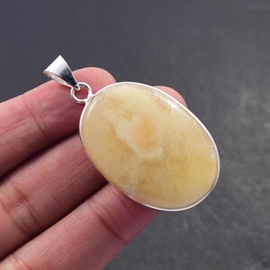 May include: Oval-shaped pendant with a pale yellow gemstone, set in a silver-colored metal frame. The gemstone has a lighter, almost peach-colored center. The pendant has a silver loop for a chain.