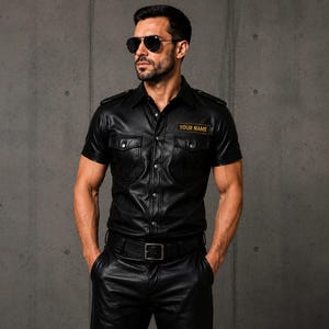 May include: Black leather short-sleeved shirt with two chest pockets and a button-down front. The shirt has a collar and epaulettes. A small patch on the chest reads "YOUR NAME". The shirt is paired with black leather trousers and a belt.