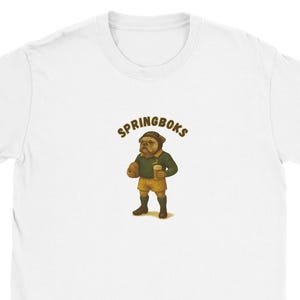 Puede incluir: Camiseta blanca con la palabra "SPRINGBOKS" sobre un bulldog de dibujos animados con uniforme de rugby y sosteniendo un balón y una bebida. El bulldog lleva una camisa verde, pantalones cortos amarillos y calcetines negros.