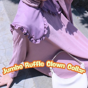 May include: A lavender-colored dress with a matching ruffled collar. The collar has a rounded shape and a frilly edge. A white handbag with a curved design is also visible. The text "Jumbo Ruffle Clown Collar" is displayed.