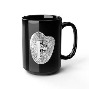 Può includere: Tazza in ceramica nera con un disegno bianco e nero della lettera "F". La lettera è all'interno di una forma ovale bianca. La tazza ha un manico grande ed è adatta per bevande calde o fredde.