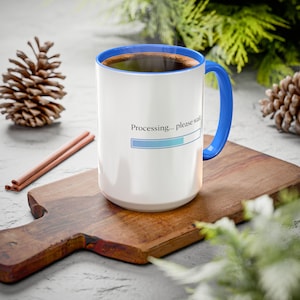 May include: White ceramic coffee mug with a blue interior and handle. The mug has the text "Processing... please wait" with a progress bar. The mug is filled with coffee and sits on a wooden cutting board.