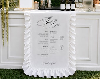 May include: A white fabric bar runner with ruffled edges featuring the text The Bar, a menu of wine, beer, spirits, non-alcoholic drinks, and signature cocktails, and the names Sarah & Erick with the date 27.07.28 printed in black ink.