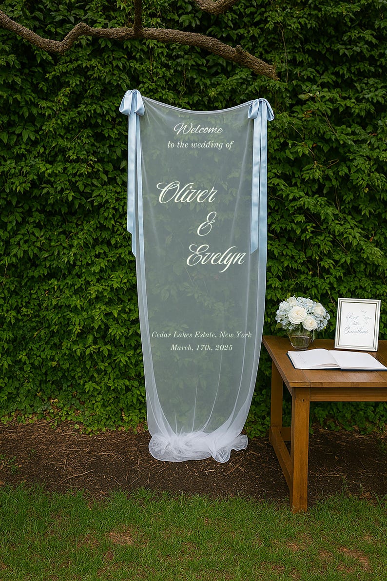 Puede incluir: Un letrero de bienvenida de boda blanco transparente con cintas azul claro. El letrero dice "Bienvenida a la boda de Oliver & Evelyn" e incluye la fecha y el lugar: Cedar Lakes Estate, Nueva York, 17 de marzo de 2025.