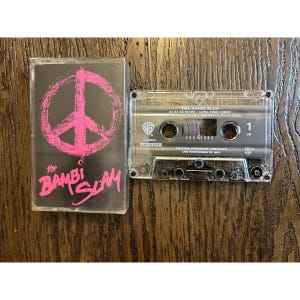 May include: A clear cassette tape with a black and pink cover. The cover features a pink peace sign and the band name "the Bambi Slam". The cassette tape is labeled with the band's name and song titles.