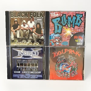 May include: Four hip-hop music CDs. The top left CD is titled "Black Folk" with the text "Broke & Po". The top right CD is titled "The Bomb" with "Hip Hop Vol. 1". The bottom left CD is titled "Raided Presents The Initiation". The bottom right CD is titled "Toolfrak".