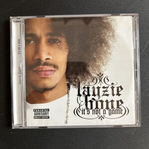 May include: A music CD in a clear plastic jewel case featuring a portrait of a person with dark curly hair on the cover. The text reads layzie bone and it's not a game, with a black and white Parental Advisory Explicit Content label.