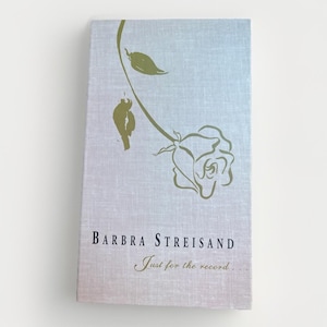 May include: A book titled "Barbra Streisand Just for the record..." features a light blue cover with a gold rose illustration. The cover has a linen texture. The book's title and author's name are in a dark blue font.