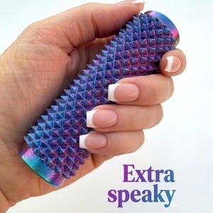 May include: A cylindrical, iridescent blue and purple object with a textured, studded surface. The text "Extra speaky" is displayed in purple and white. The object is held in a hand with manicured nails.