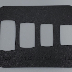 May include: A black plastic nail sizing guide with four rectangular cutouts of varying sizes. The sizes are labeled as 1.50, 1.25, 1.125, and 1.00. The guide is used for nail sizing.
