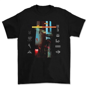Op de afbeelding: Zwart T-shirt met een grafisch ontwerp. Het ontwerp toont de tekst "DEPECHE MODE BLACK CELEBRATION" in geel, een stadsgezicht met rode en blauwe tinten en diverse symbolen.