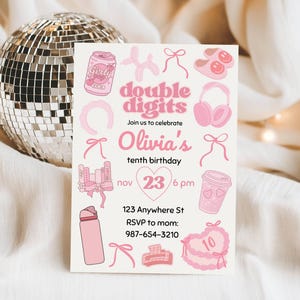 May include: A pink and white invitation card with the text "double digits" and "Olivia's tenth birthday." The card features illustrations of a soda can, headphones, and a cake. A disco ball sits behind the card.