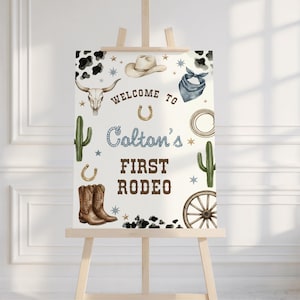 May include: A western-themed sign on an easel, featuring a cowboy hat, boots, and a steer skull. The sign reads "Welcome to Colton's First Rodeo" in a mix of fonts and colors, with decorative stars and cacti.