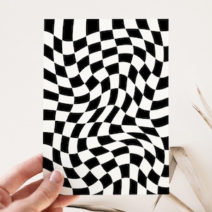 Puede incluir: Una tarjeta rectangular con un patr&oacute;n de tablero de ajedrez en blanco y negro distorsionado y ondulado. La tarjeta es sostenida por una mano sobre un fondo neutro. El patr&oacute;n de tablero de ajedrez crea una ilusi&oacute;n visual.