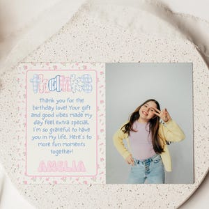 May include: A personalized thank you card with the name "Amelia" in pink bubble letters. The card features a photo of a smiling person and the word "thanks" in a colorful, patterned font. The card is on a decorative, speckled surface.