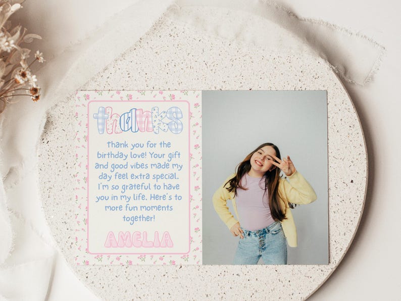 May include: A personalized thank you card with the name "Amelia" in pink bubble letters. The card features a photo of a smiling person and the word "thanks" in a colorful, patterned font. The card is on a decorative, speckled surface.
