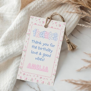 May include: A gift tag with a floral border and the word "THANKS" in a colorful, patterned font. The tag includes the message "thank you for the birthday love & good vibes!" and the name "AMELIA". A natural twine string is attached.