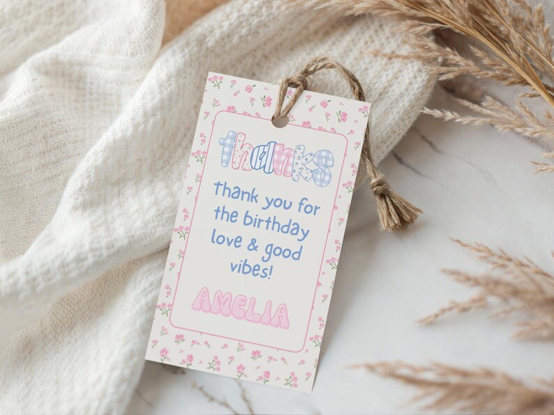 May include: A gift tag with a floral border and the word "THANKS" in a colorful, patterned font. The tag includes the message "thank you for the birthday love & good vibes!" and the name "AMELIA". A natural twine string is attached.