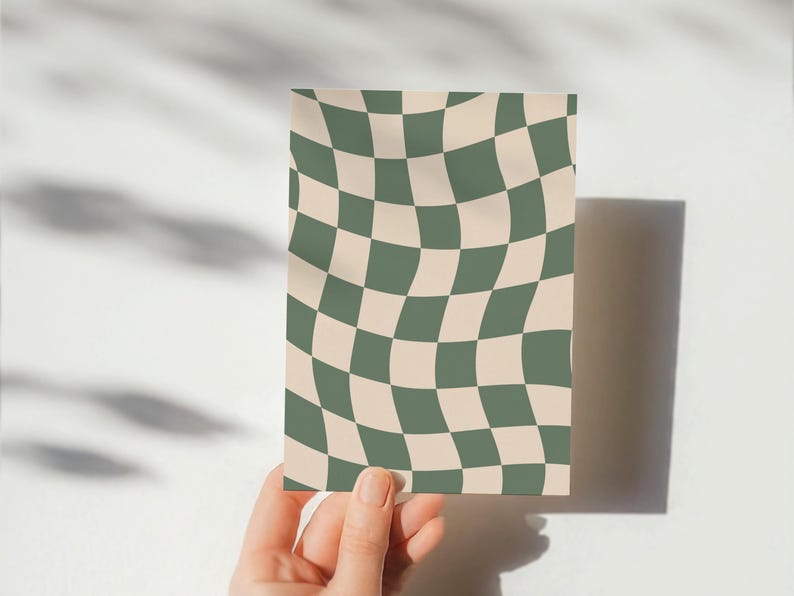 May include: A rectangular card with a wavy checkerboard pattern in olive green and beige. The card is held by a hand against a white background, with shadows cast on the surface.