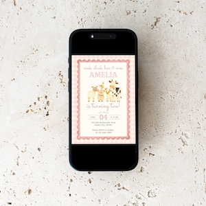 May include: A smartphone displays a pink and cream-colored birthday invitation. The invitation features illustrations of farm animals and the text "Amelia is turning two!" with the date June 4th.