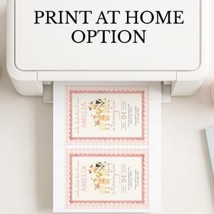 May include: A white printer printing two invitations with a pink border and a farm animal theme. The invitations read "Amelia is turning two!" and include the text "Print at Home Option" at the top.