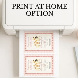 May include: A white printer is printing two invitations with a pink border and a farm animal theme. The text "PRINT AT HOME OPTION" is above the printer. A small plant, a pink mug, and a notebook are on the white surface.