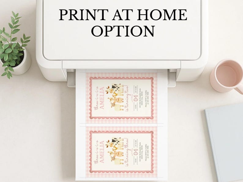 May include: A white printer is printing two invitations with a pink border and a farm animal theme. The text "PRINT AT HOME OPTION" is above the printer. A small plant, a pink mug, and a notebook are on the white surface.