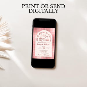 Pu&ograve; includere: Uno smartphone mostra un invito a un baby shower con un motivo a quadretti rossi. L'invito include il testo "You're Invited to a Baby-Q" e i dettagli del baby shower di Jessica Williams. Il telefono &egrave; su una superficie bianca.
