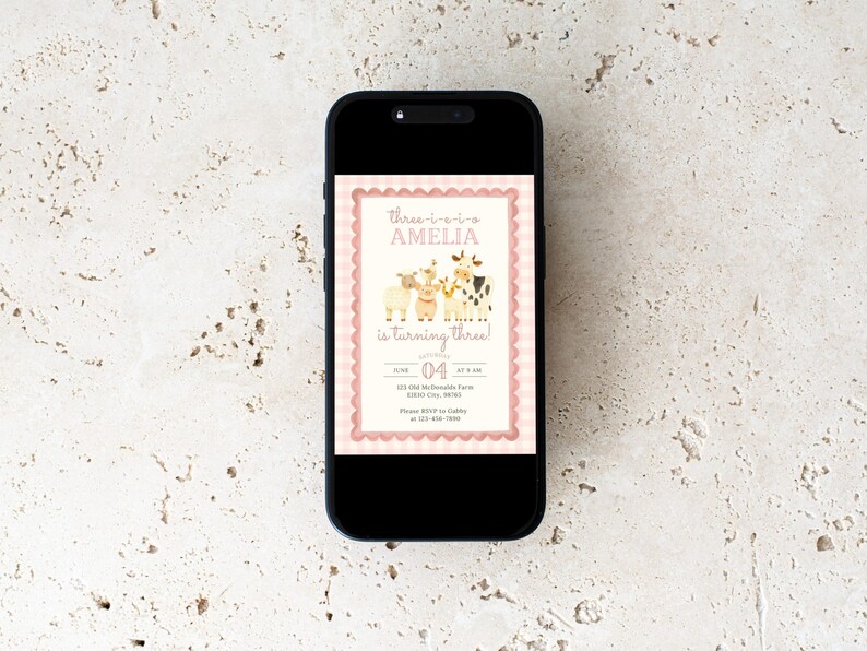 May include: A smartphone displays a pink and cream birthday invitation. The invitation features illustrations of farm animals and the text "three-o-two Amelia is turning three!" The date is June 4th.