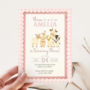 Puede incluir: Una tarjeta de invitación rosa con estampado de cuadros vichy y borde festoneado. La tarjeta presenta ilustraciones de animales de granja y el texto "three-i-e-i-o AMELIA is turning three!" con la fecha y hora de la fiesta.