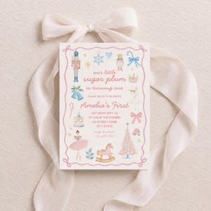 May include: A rectangular invitation card with a pink rope-style border featuring watercolour illustrations of a nutcracker, snowflake, teddy bear, candy cane, crown, carousel, ballerina, and pink Christmas tree with text: our little sugar plum is turning one.