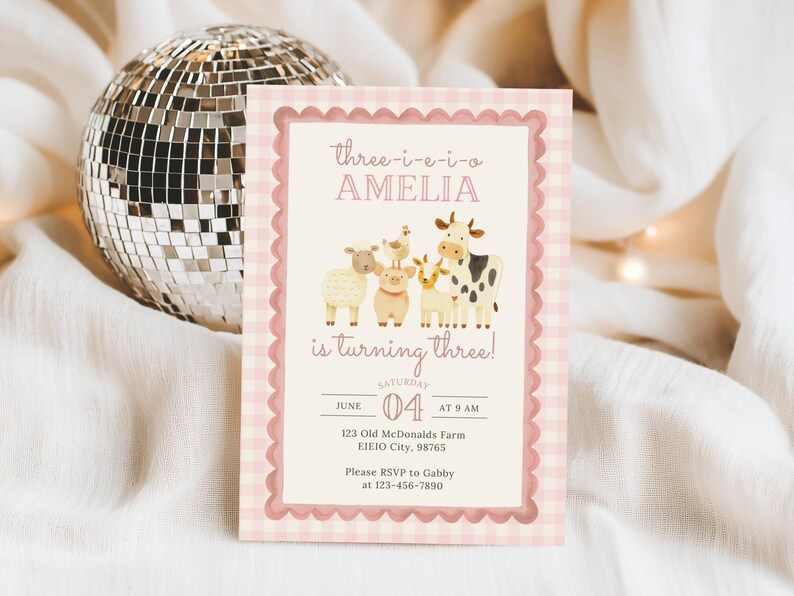 Close up of girl barnyard invite with pink barn, farm animals, and Three I E I O wording for cute farm themed 3rd birthday party, printable digital template.