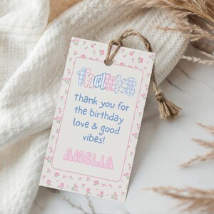 Op de afbeelding: Een cadeaulabel met een bloemenrand en het woord "THANKS" in een kleurrijk, speels lettertype. Het label bevat de boodschap "thank you for the birthday love & good vibes!" en de naam "AMELIA". Een natuurlijke touwtje is bevestigd.