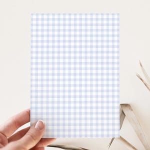 May include: A rectangular card with a light blue and white gingham pattern is held by a hand. The card is centered in the frame, with the gingham pattern covering the entire surface. The background is a neutral color.