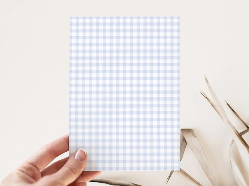 May include: A rectangular card with a light blue and white gingham pattern is held by a hand. The card is centered in the frame, with the gingham pattern covering the entire surface. The background is a neutral color.